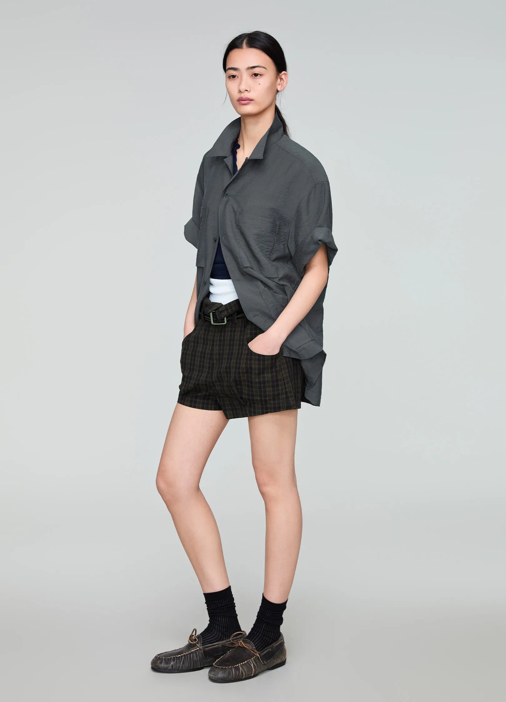 Person wearing a dark gray shirt and black plaid shorts on a light gray background